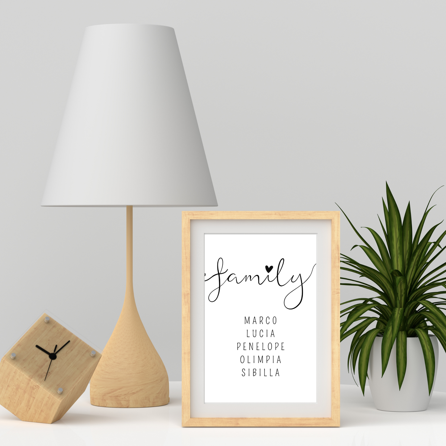 Grafica stampabile FAMILY personalizzabile con il nome dei membri della famiglia incorniciata e appoggiata su piano vicino ad una lampada dai toni naturali.