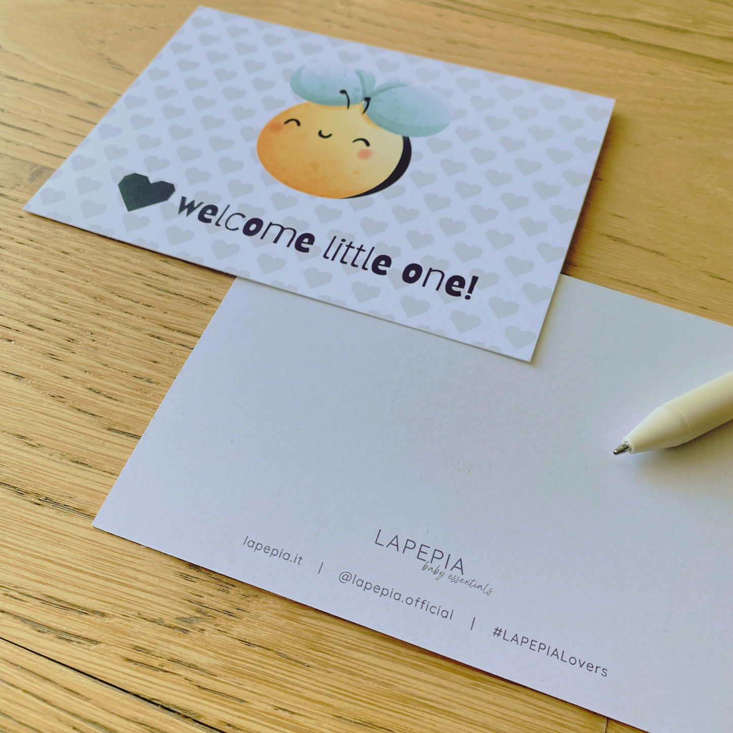 Cartolina di auguri "welcome little on" con ape acquerellata su fondo a cuoricini, fronte/retro