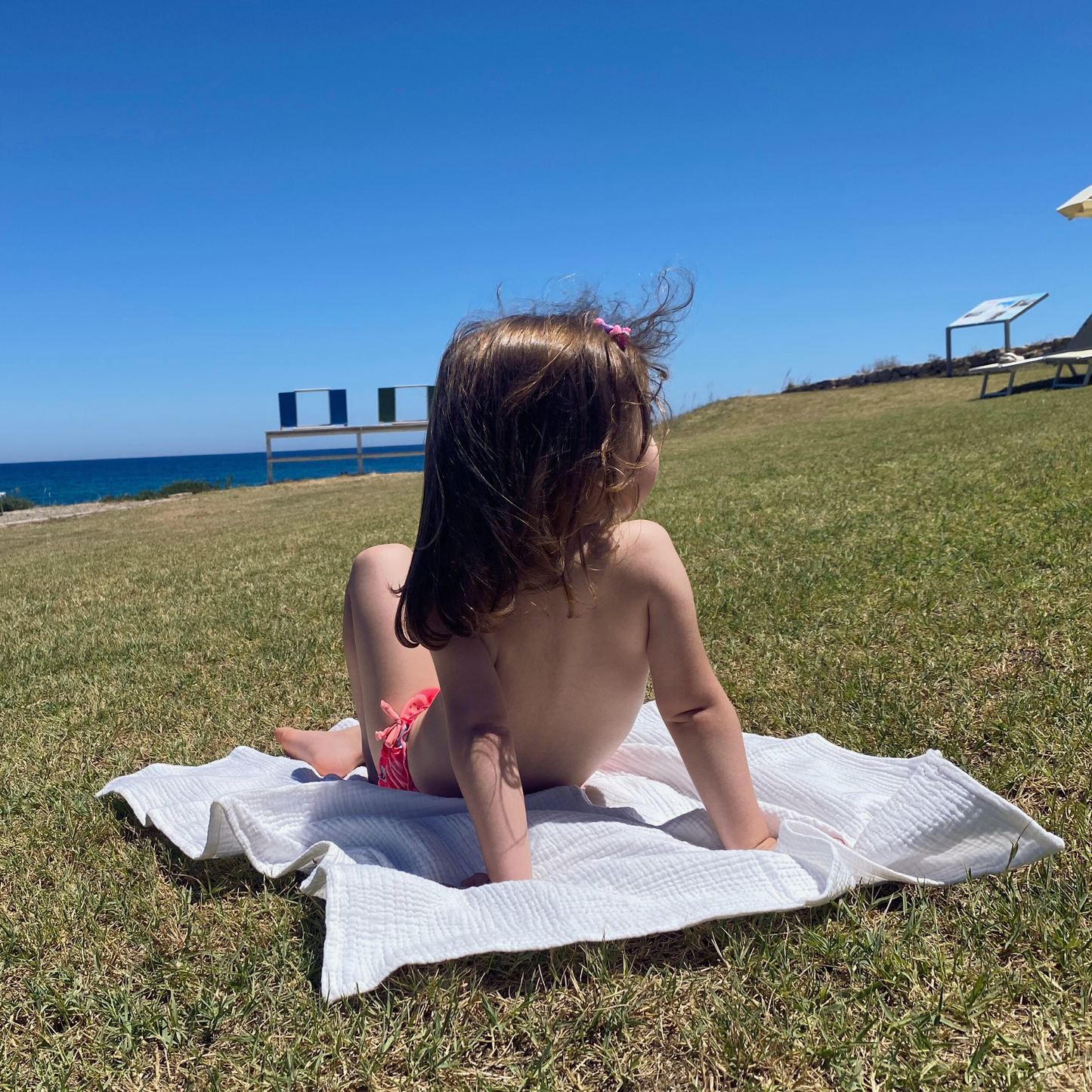 Copertina in mussola di cotone nel colore Cream appoggiata su prato come telo con bambina di spalle.