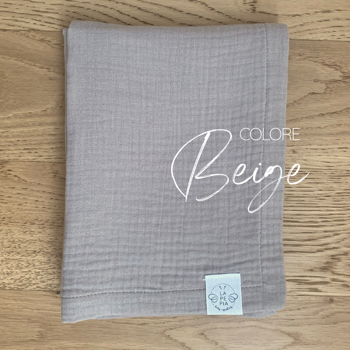 Copertina in mussola di cotone nel colore Beige piegata e appoggiata su piano in legno.