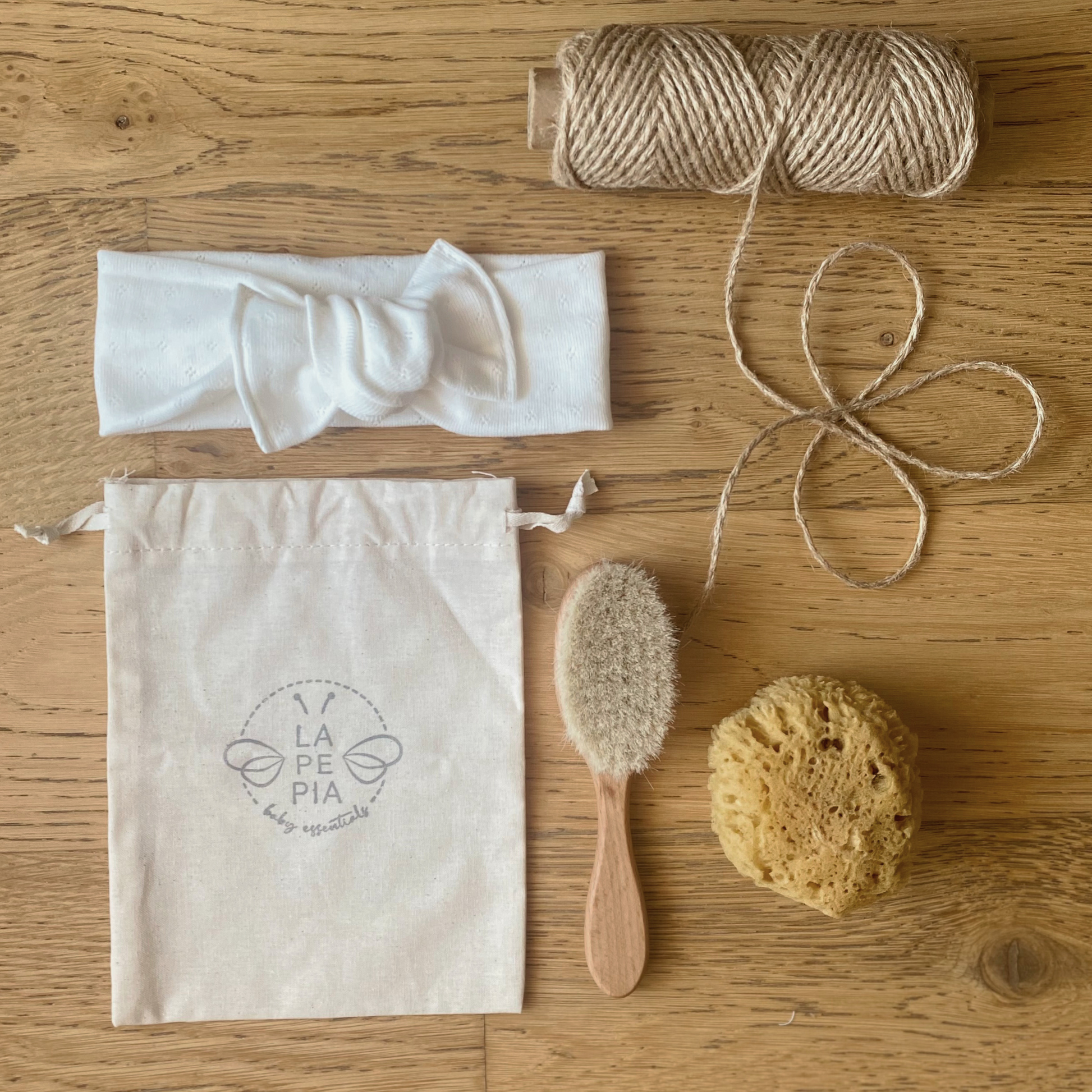 Spazzola FSC e setole naturali, spugna di mare, pouch multiuso, fascia per capelli fotografati su piano in legno. 