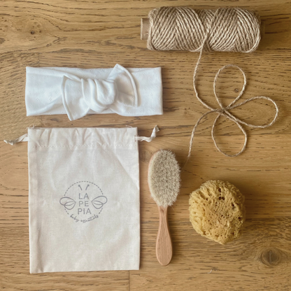 Spazzola FSC e setole naturali, spugna di mare, pouch multiuso, fascia per capelli fotografati su piano in legno. 