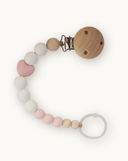 Catenella portaciuccio in silicone rosa cipria e bianco con dettaglio a cuore e clip in legno per neonata.