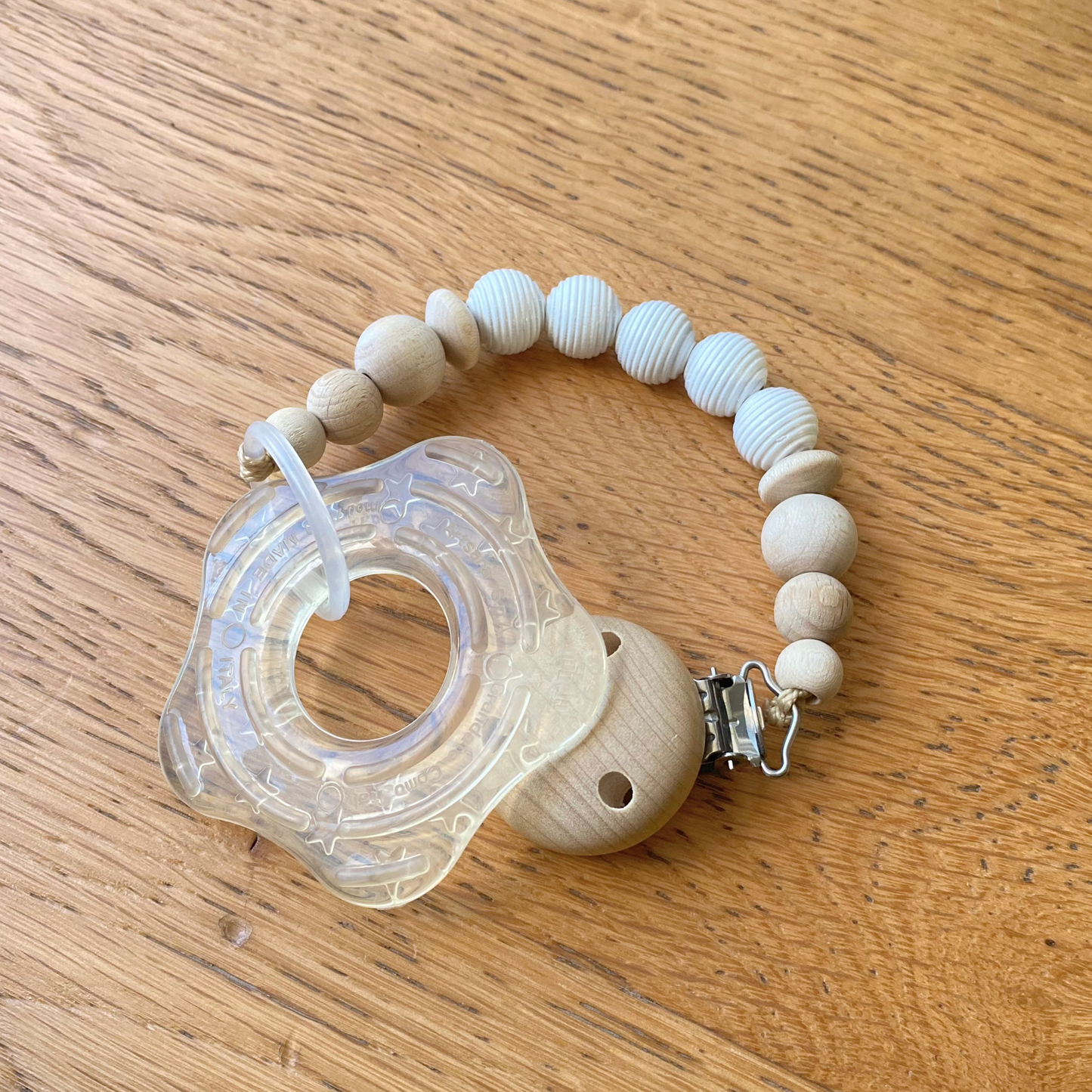 Catenella portaciuccio LAPEPIA con perle in legno naturale e legno bianco agganciato su giochino.