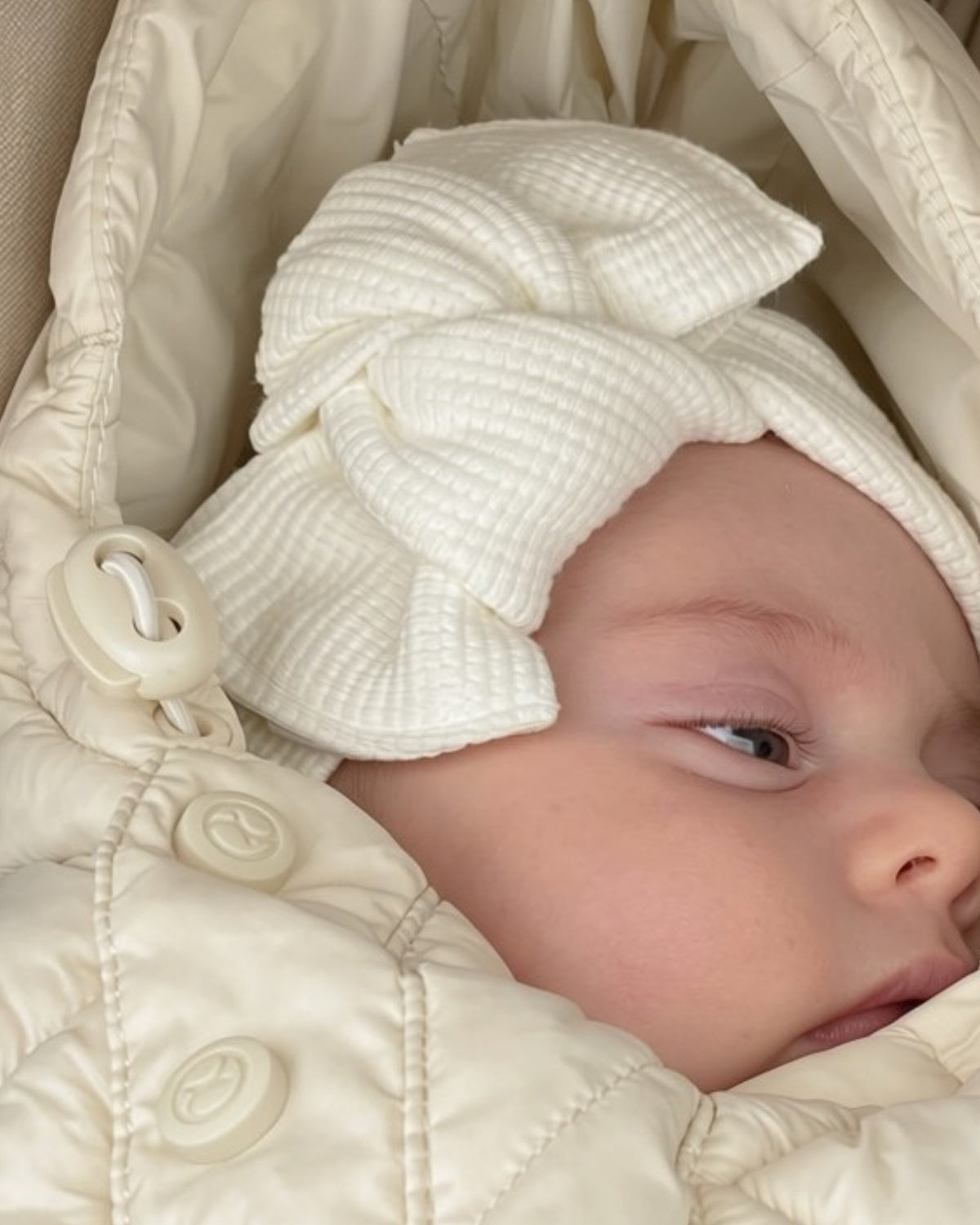 Dettaglio di fascia per capelli da neonata colore bianco lavorazione nido d'ape indossata nel sacco nanna invernale