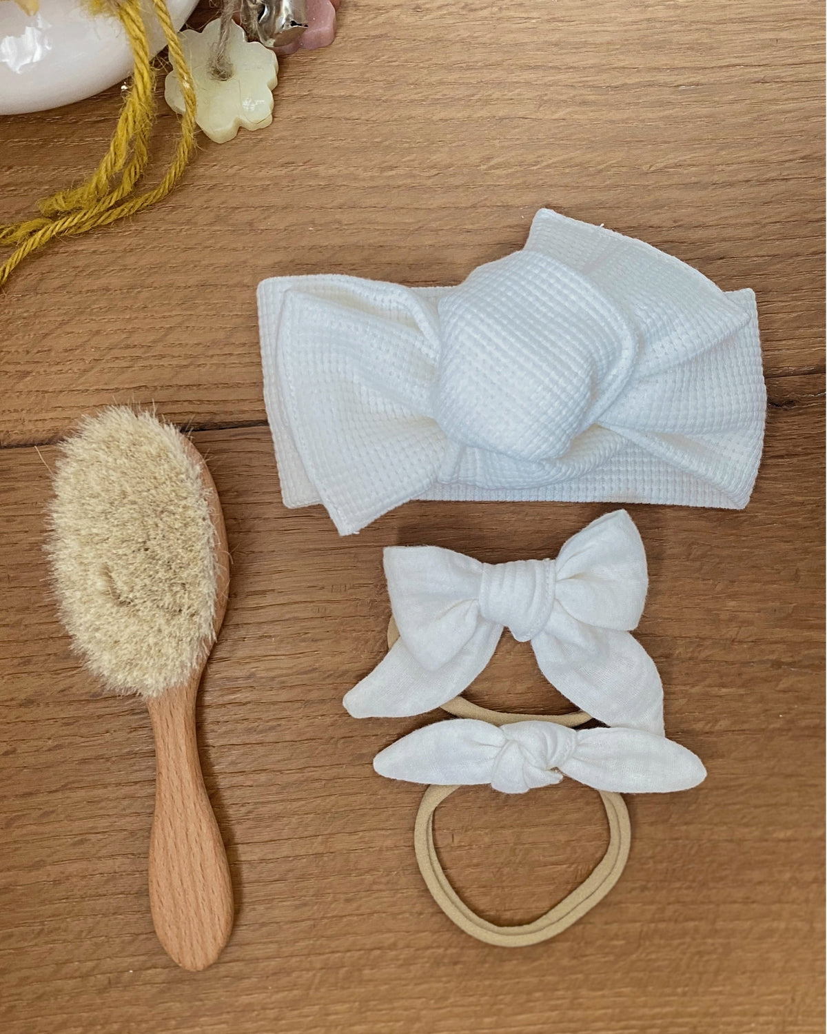 Flatlay con fascia per capelli nido d'ape colore panna, elastico e spazzola per neonato in legno