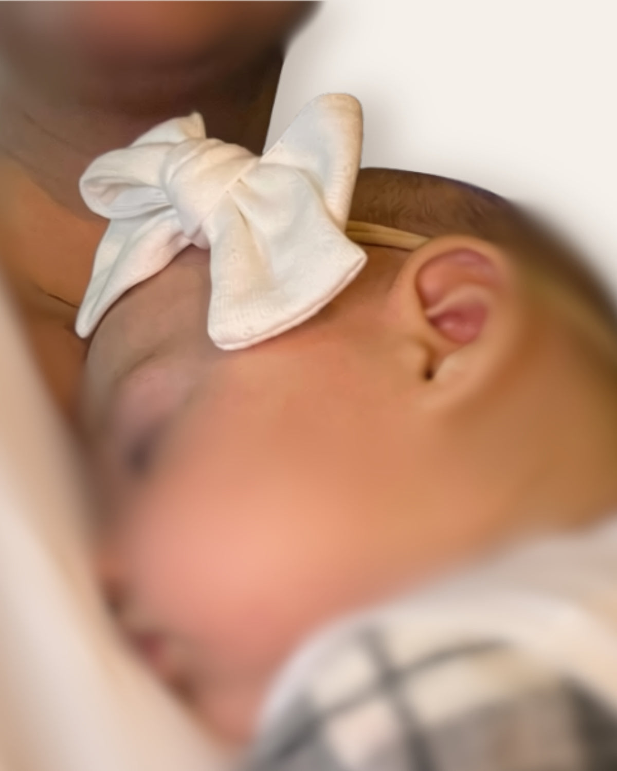 Neonata che dorme indossando una fascia morbida per capelli con fiocco Classic Bow color panna in cotone.