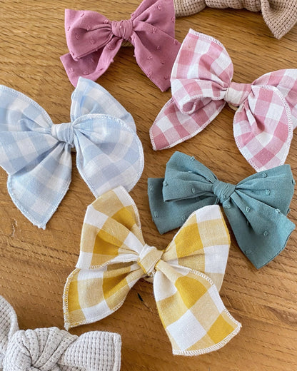 Collezione di fiocchi per capelli da bambina e neonata fatti a mano in cotone, in varie tinte unite e fantasie a quadretti vichy.