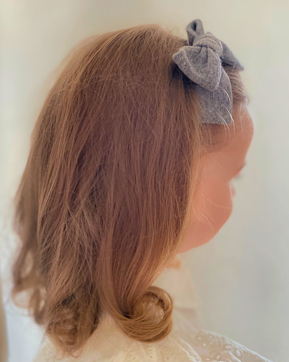 Particolare di una bambina con fiocco per capelli grigio annodato a mano applicato lateralmente sulla chioma.