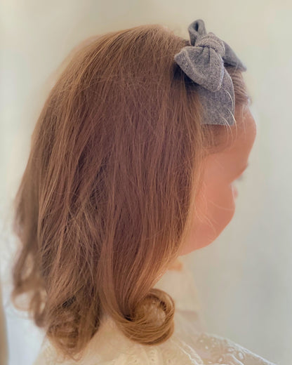 Particolare di una bambina con fiocco per capelli grigio annodato a mano applicato lateralmente sulla chioma.