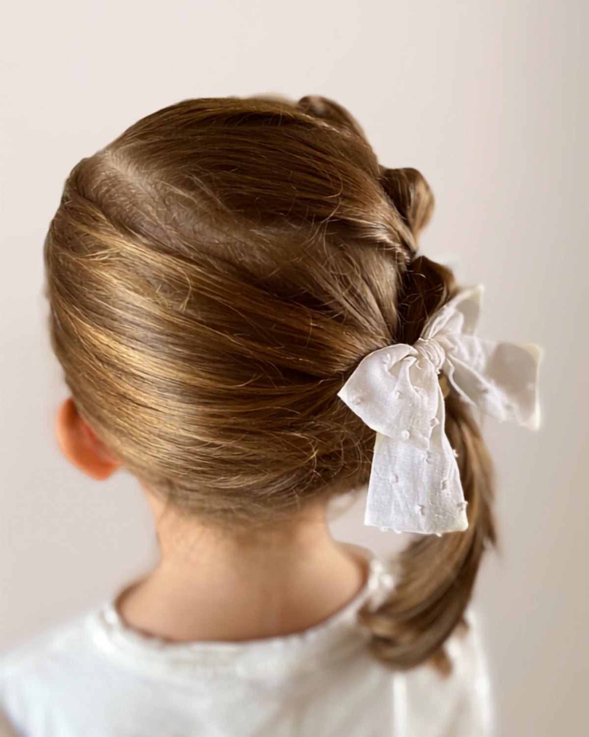 Acconciatura elegante da bambina decorata con fiocco per capelli bianco in cotone lavorato plumetis.