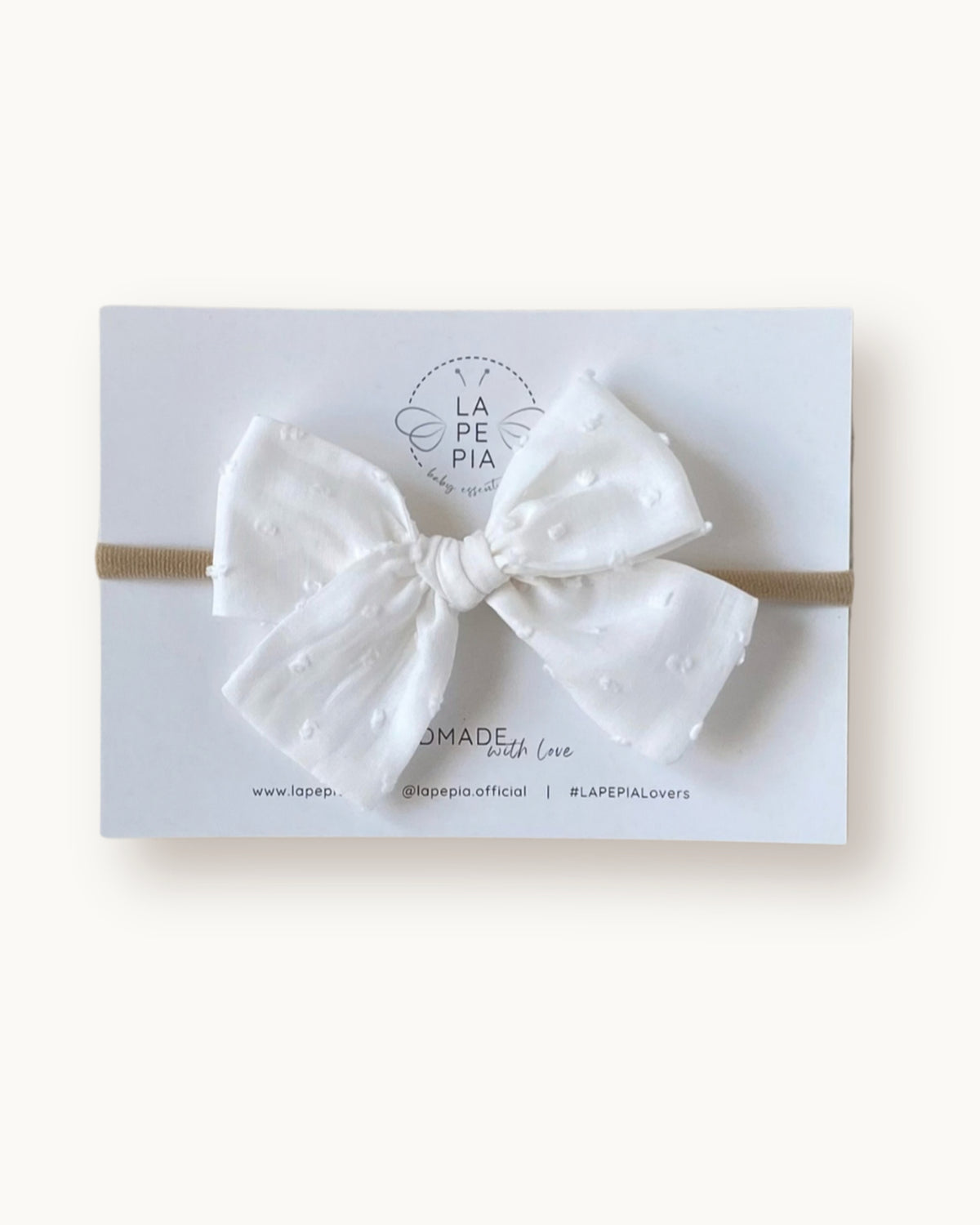 Fiocco per capelli Classic Bow in voile di cotone plumetis soft white con pallini in rilievo, montato su fascia morbida per neonata.