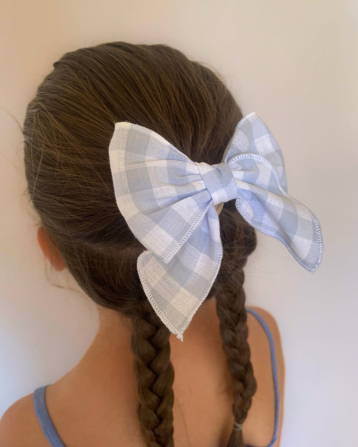Acconciatura con trecce da bambina arricchita da un maxi fiocco per capelli a quadretti vichy azzurro e bianco.
