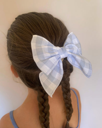 Acconciatura con trecce da bambina arricchita da un maxi fiocco per capelli a quadretti vichy azzurro e bianco.