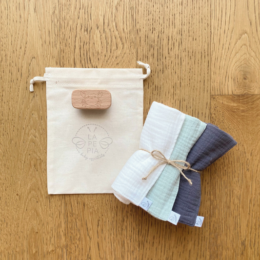 Kit igiene neonato con lavette in mussola bio, spazzolina in legno per unghie e sacchetto.