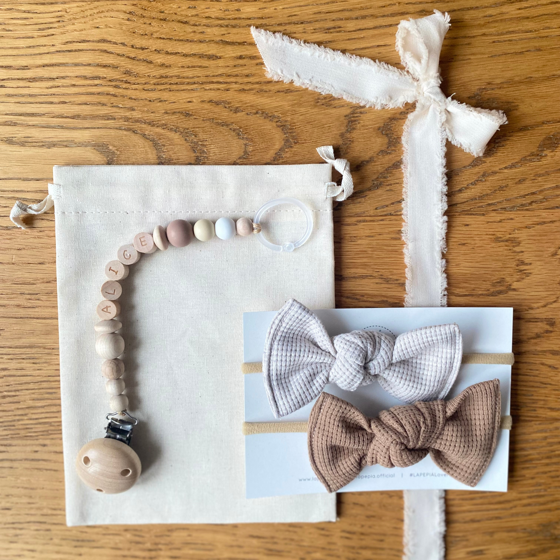 Set regalo Little Wonder Box 'NameIT & LoveIT' nella variante colore Mocha Bloom, composto da 2 fiocchi per capelli, catenella portaciuccio personalizzabile con nome e  sacchettino protettivo in cotone. LAPEPIA.