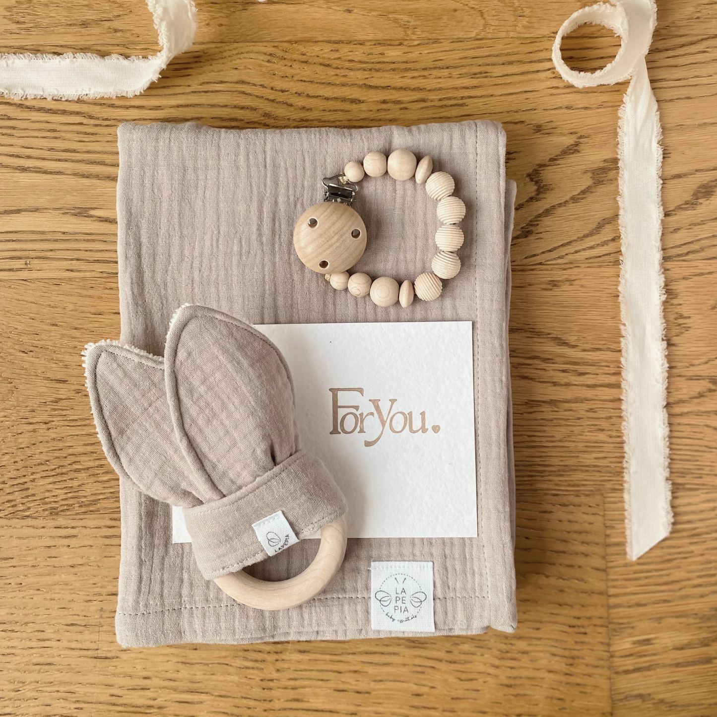 Set regalo Little Wonder Box 'NewBorn Essentials' nella variante Beige composto da copertina in mussola beige, Dou Dou beige con anello dentizione, catenella portaciuccio honey maple e sacchettino protettivo in cotone. LAPEPIA.