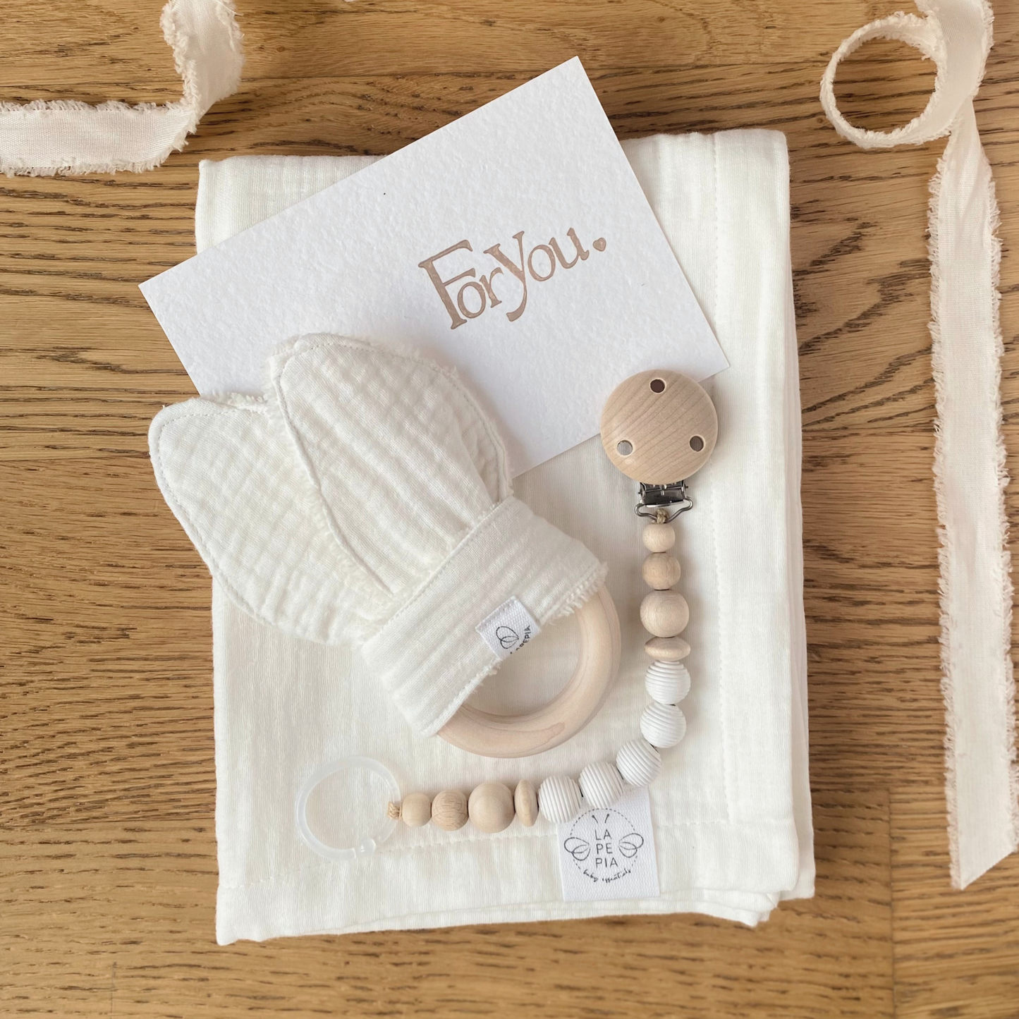 Set regalo Little Wonder Box 'NewBorn Essentials' nella variante Cream composto da copertina in mussola cream, Dou Dou cream con anello dentizione, catenella portaciuccio snowbound e sacchettino protettivo in cotone. LAPEPIA.