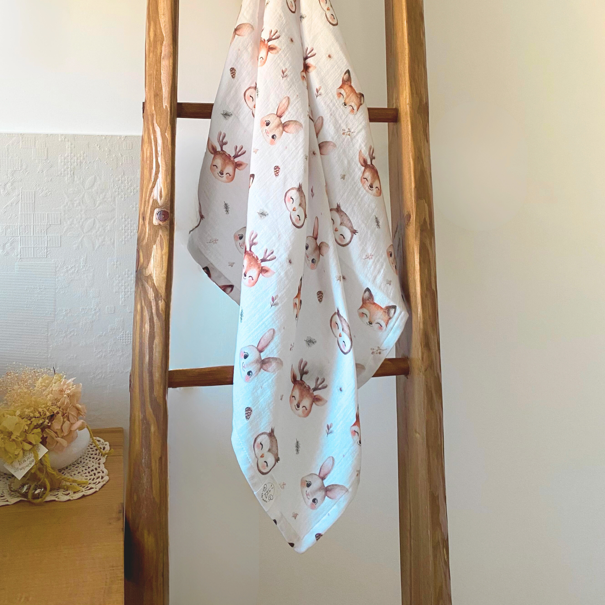 Mussola di cotone 70x70 variante Bosco Incantato appesa a una scala in legno appoggiata al muro, ambientazione elegante e naturale.