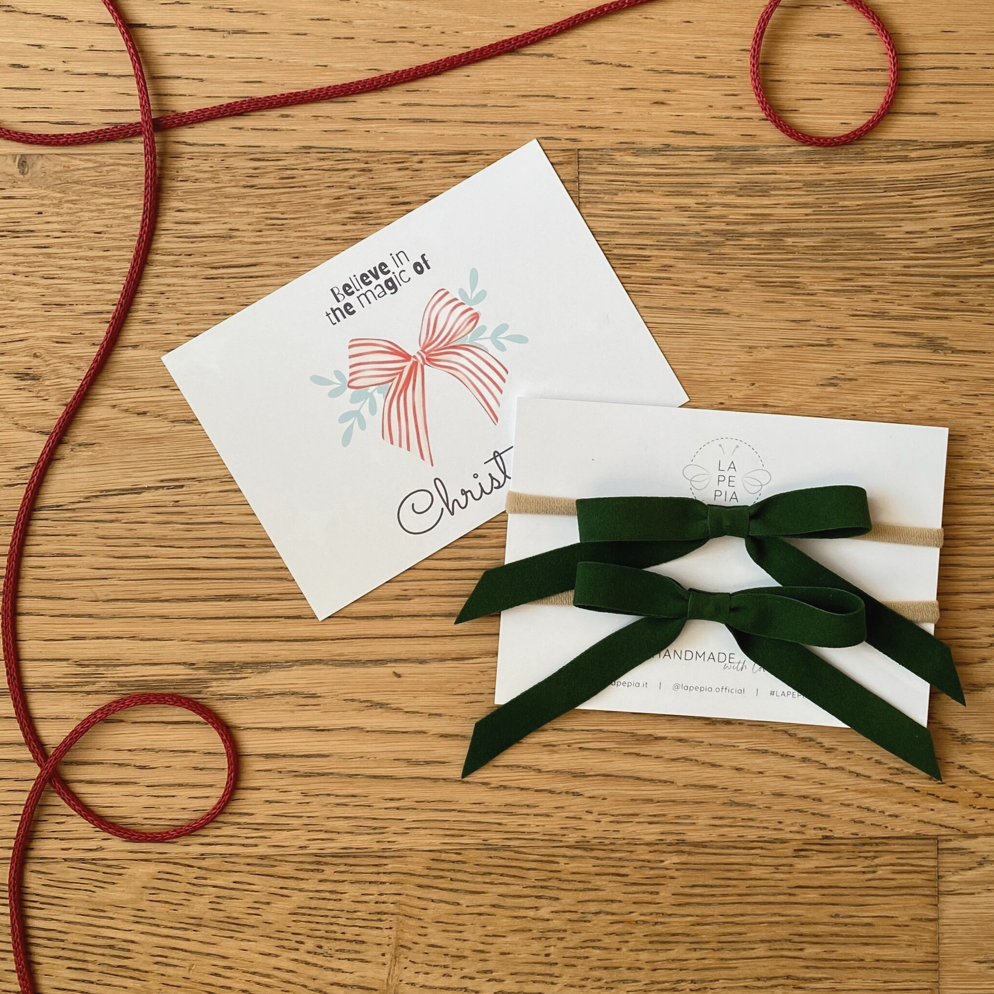 Fiocchi di velluto verde del set Velvet Holly accanto alla cartolina con grafica natalizia, ideale come regalo raffinato per il Natale. LAPEPIA.