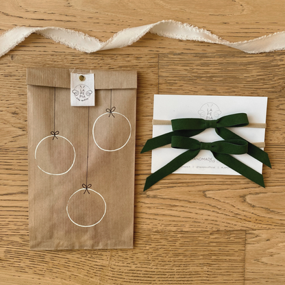 Fiocchi di velluto verde del set Velvet Holly, confezionati in un sacchetto di carta kraft decorato a mano, perfetto come idea regalo di Natale. LAPEPIA.